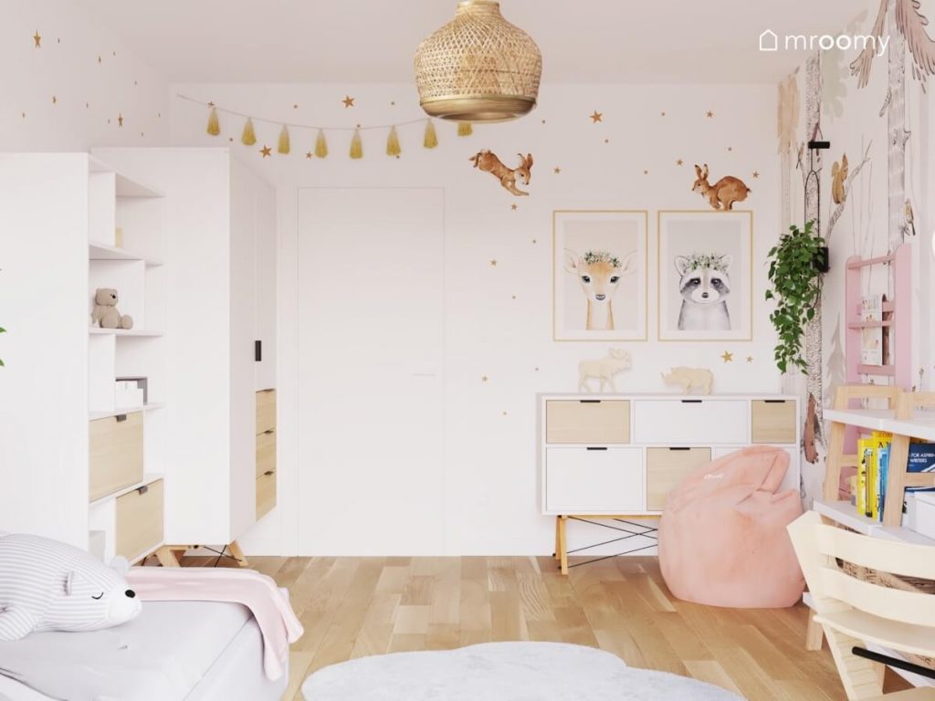 Biały pokój małej dziewczynki a w nim biało drewniane meble różowa pufa oraz ściany ozdobione naklejkami i plakatami ze zwierzętami
