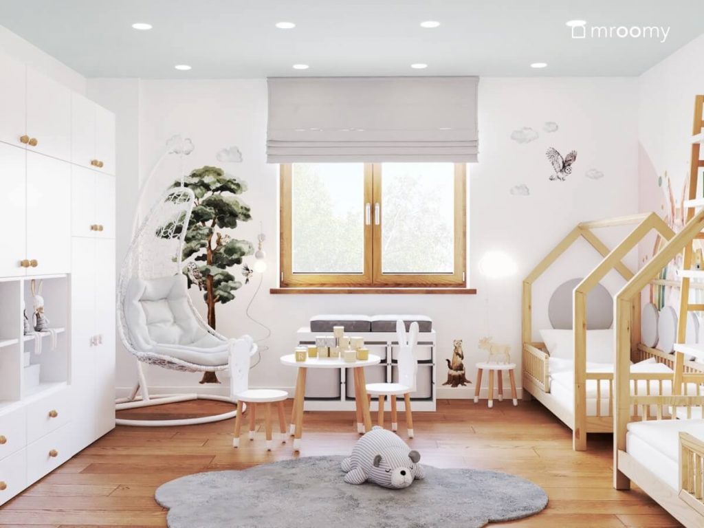 Biały pokój dla dwulatków z błękitnym sufitem oraz biało drewnianymi meblami fotelem wiszącym oraz naklejkami w kształcie chmue