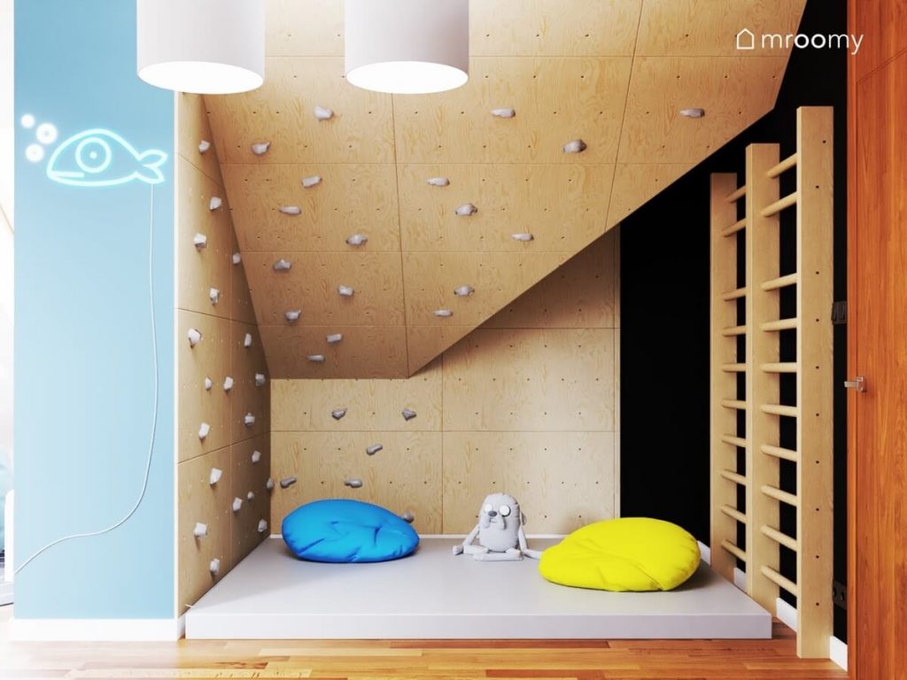 Strefa rozrywki w postaci drewnianej ścianki wspinaczkowej na skosie oraz drabinek gimnastycznych oraz kolorowych puf i szarego materaca gimnastycznego w pokoju dla rodzeństwa