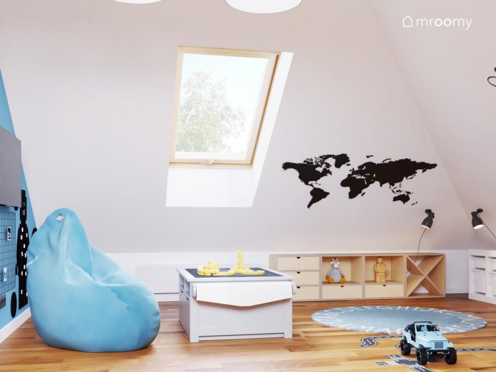 Biały skos w pokoju zabaw dla dziewczynek i chłopca a na nim naklejka w kształcie mapy świata a pod spodem drewniane szafki a na podłodze niebieski dywan z alfabetem i błękitna pufa