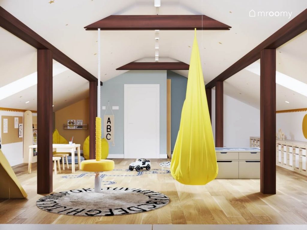 Żółty fotel wiszący oraz żółta huśtawka ring a na podłodze dywan z alfabetem w poddaszowej bawialni rodzeństwa