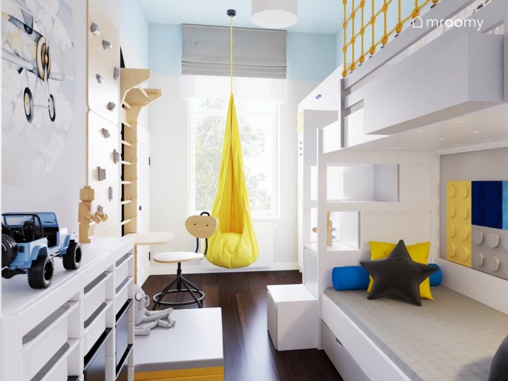 Biało niebieski pokój przedszkolaka a w nim biała antresola żółty fotel kokon oraz drabinka gimnastyczna i ścianka wspinaczkowa