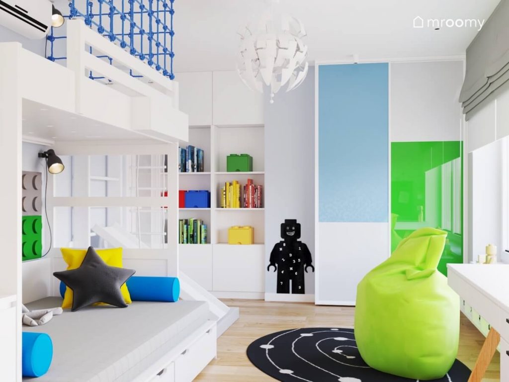 Jasny pokój dla chłopca a w nim białe meble tablica kredowa w kształcie ludzika Lego zielona pufa oraz szafa z zielonym i niebieskim frontem