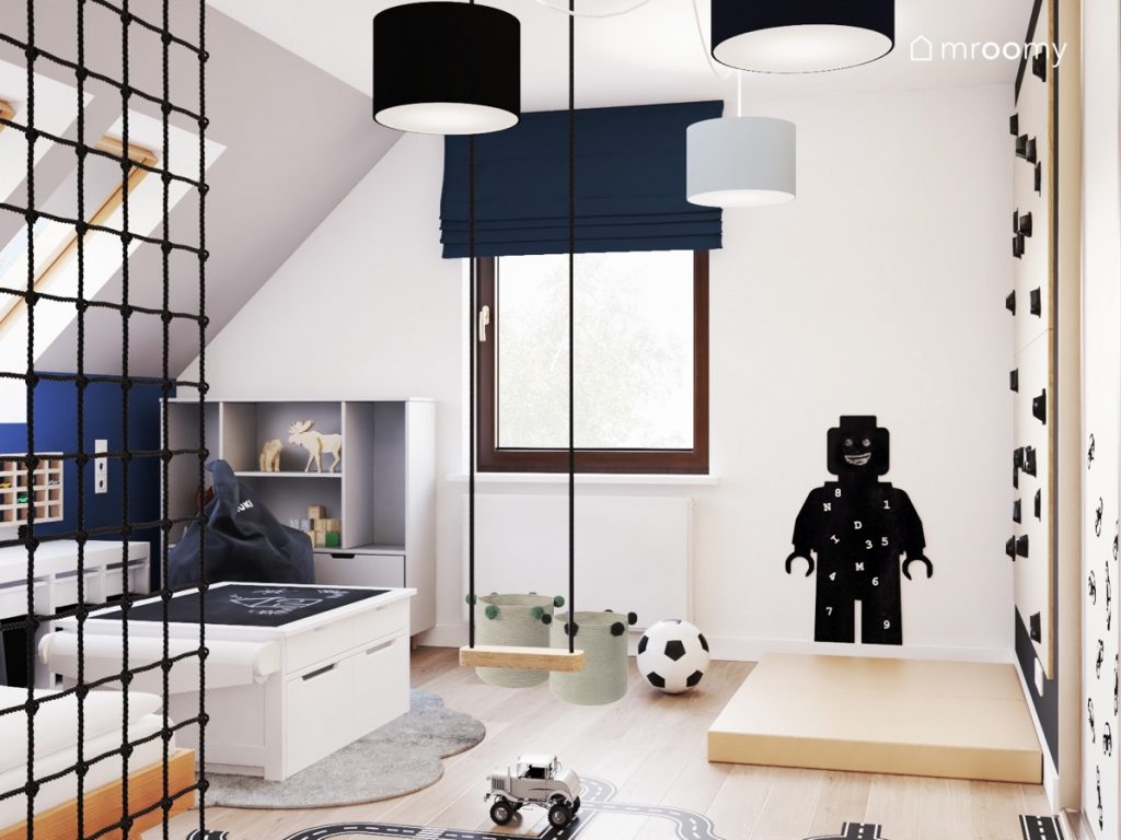 Poddaszowy pokój dla chłopca a w nim białe i szare meble prosta huśtawka wisząca tablica kredowa w kształcie ludzika Lego oraz lampa z abażurami w trzech kolorach