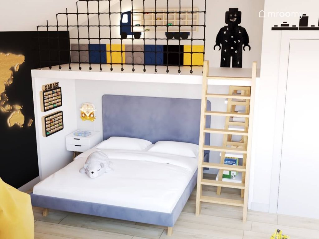 Duże tapicerowane łóżko w pokoju dla chłopca a na ścianie półki na samochody a nad nim antresola z tablicą kredową w kształcie ludzika Lego i jeszcze jedna półka na samochody