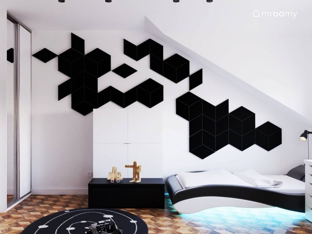 Łóżko w oryginalnym kształcie a nad nim geometryczna kompozycja z czarnych paneli w pokoju nastolatka