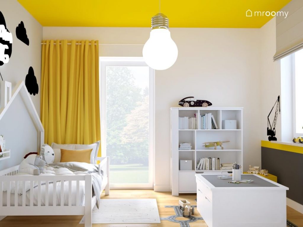 Jasny pokój dla dwulatka z żółtym sufitem i zasłonami a także z białymi meblami naklejką podłogową w kształcie jezdni i dużą żarówką na suficie