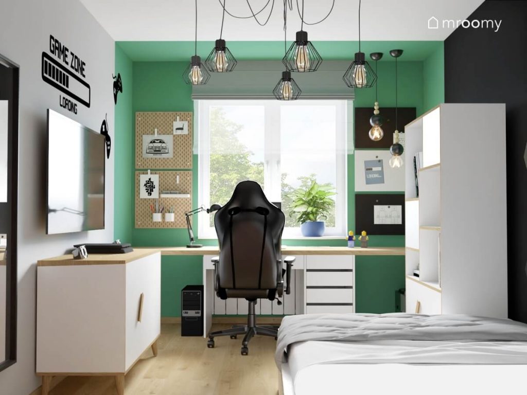Szaro biało zielono czarny pokój nastolatka a w nim biało drewniane meble organizery ścienne fotel gamingowy oraz ozdobna lampa sufitowa z geometrycznymi kloszami