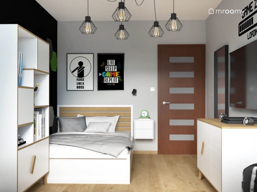Biało drewniane łóżko a nad nim gamingowe plakaty a obok ścienna szafka nocna z zegarem w pokoju dla nastolatka