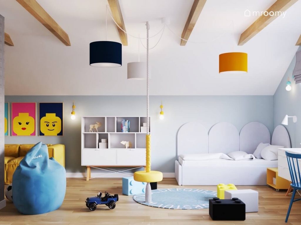 Biało szary pokój dla chłopca w wieku szkolnym a w nim białe meble żółta huśtawka ring pufki w kształcie klocków dywan z alfabetem błękitna pufa oraz plakaty z ludzikami Lego
