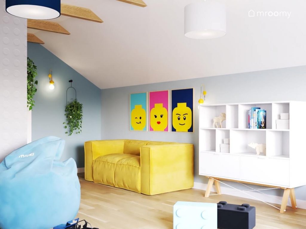 Żółta kanapa a nad nią plakaty z ludzikami Lego a obok biały regał na drewnianych nogach i kwietnik w niebiesko biało szarym poddaszowym pokoju chłopca