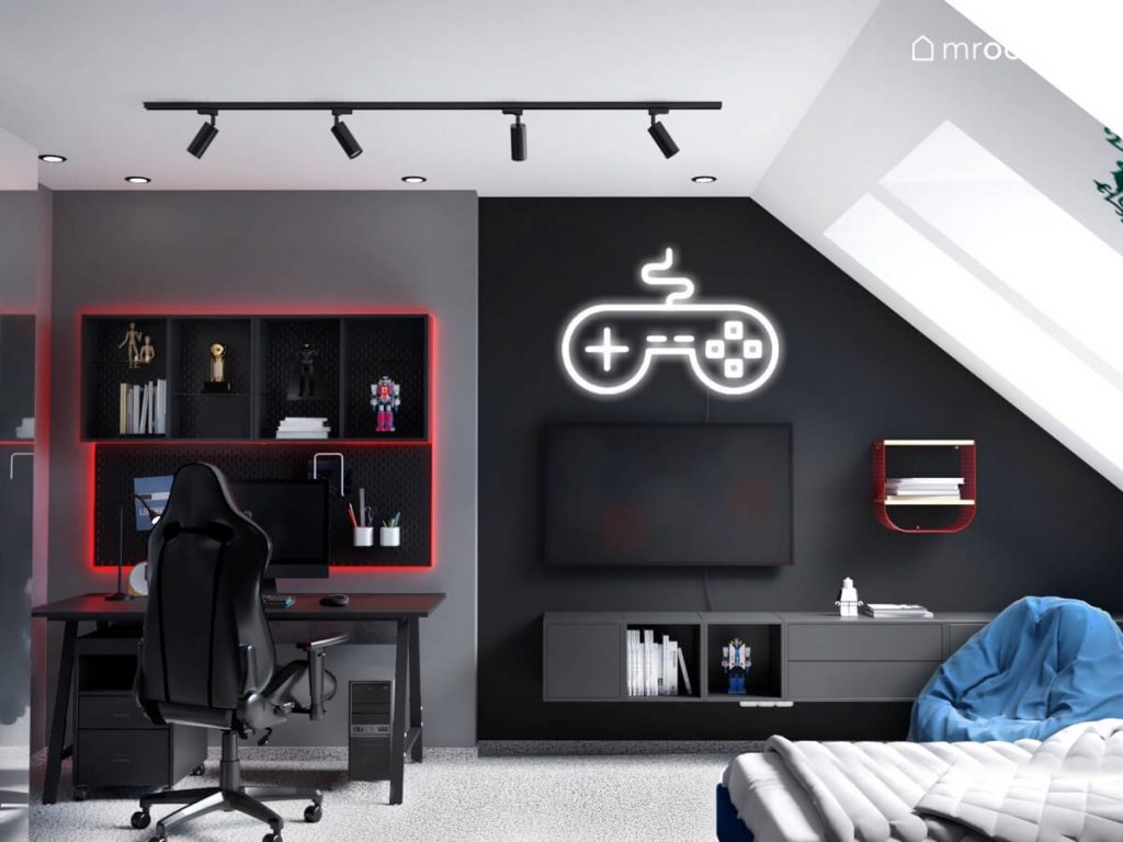 Biurko z fotelem gamingowym oraz podświetlanymi na czerwono organizerami i półkami a obok telewizor ledon w kształcie pada oraz szafki ścienne w pokoju chłopca