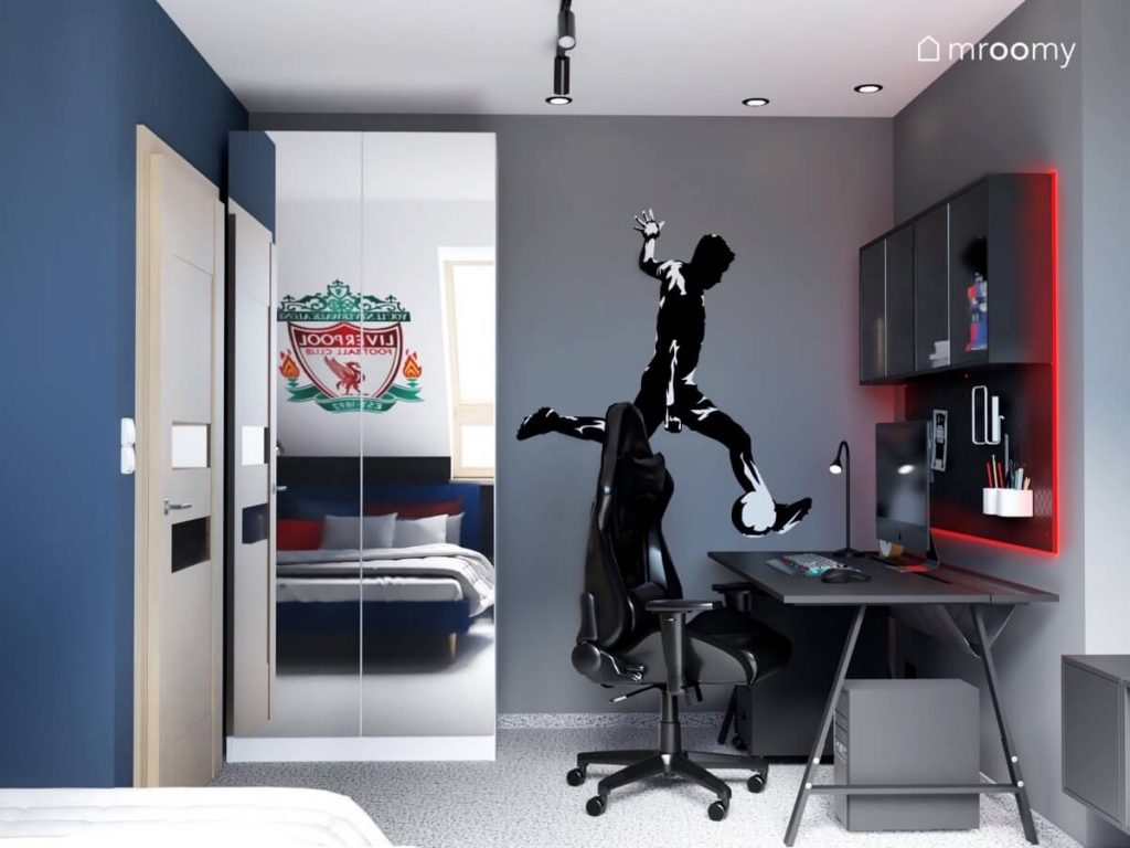Szafa z lustrzanymi frontami a obok naklejka w kształcie piłkarza na szarej ścianie w pokoju chłopca fana piłki nożnej i gier wideo