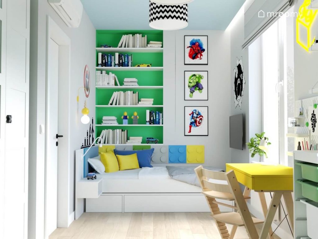 Zielona wnęka z półkami na książki a także plakaty z bohaterami Marvela a pod nimi łóżko uzupełnione panelami w kształcie klocków w różnych kolorach