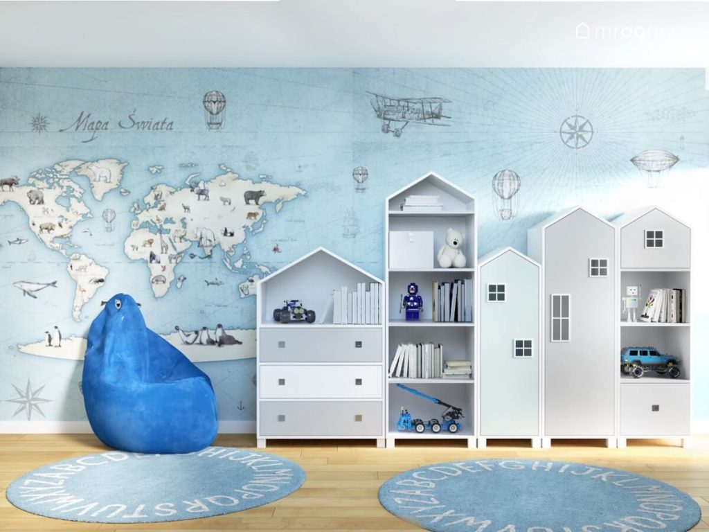 Wieloformatowa tapeta z mapą świata oraz niebieska pufa i meble w kształcie domków a na podłodze dywany z alfabetem w pokoju dwóch chłopców