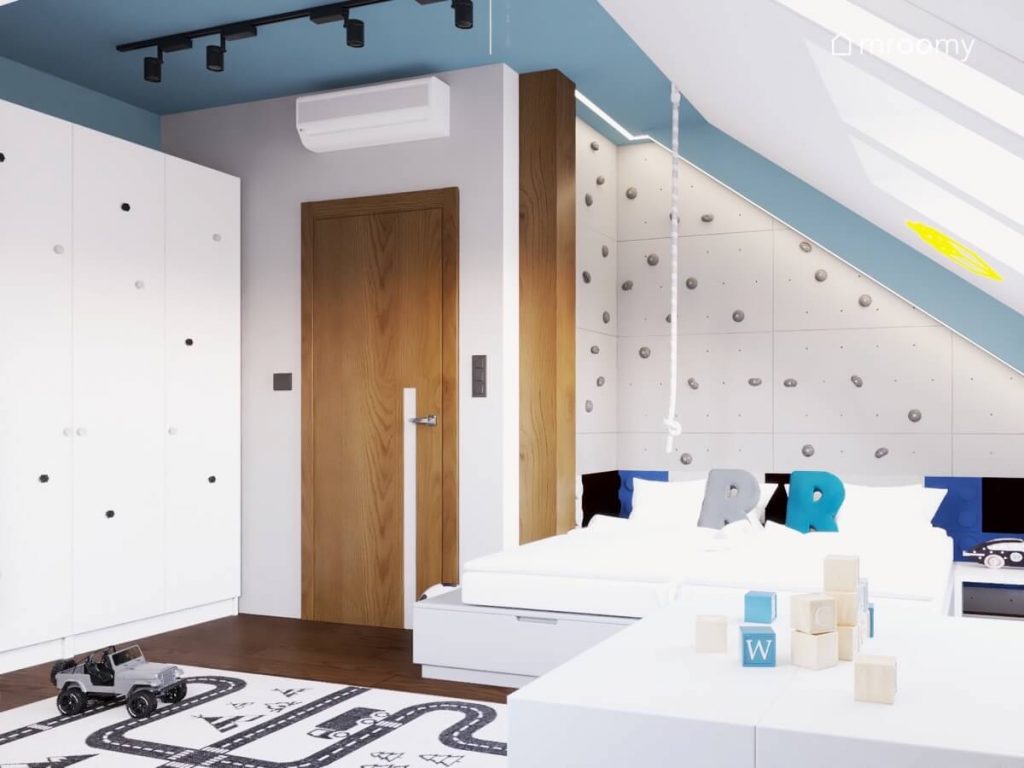 Biało niebieski poddaszowy pokój dwóch chłopców w wieku przedszkolnym a w nim duża biała szafa oraz ścianka wspinaczkowa za łóżkami