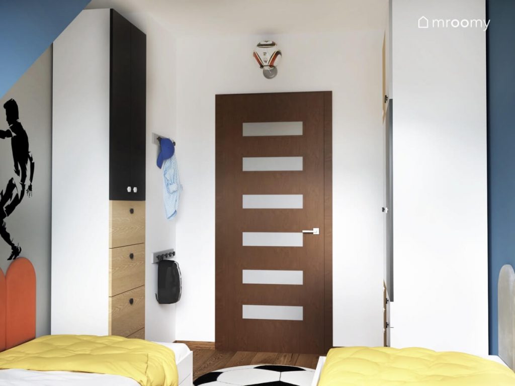 Biało szaro niebieska sypialnia dwóch chłopców a w niej biało czarno drewniane szafy a nad drzwiami piłka