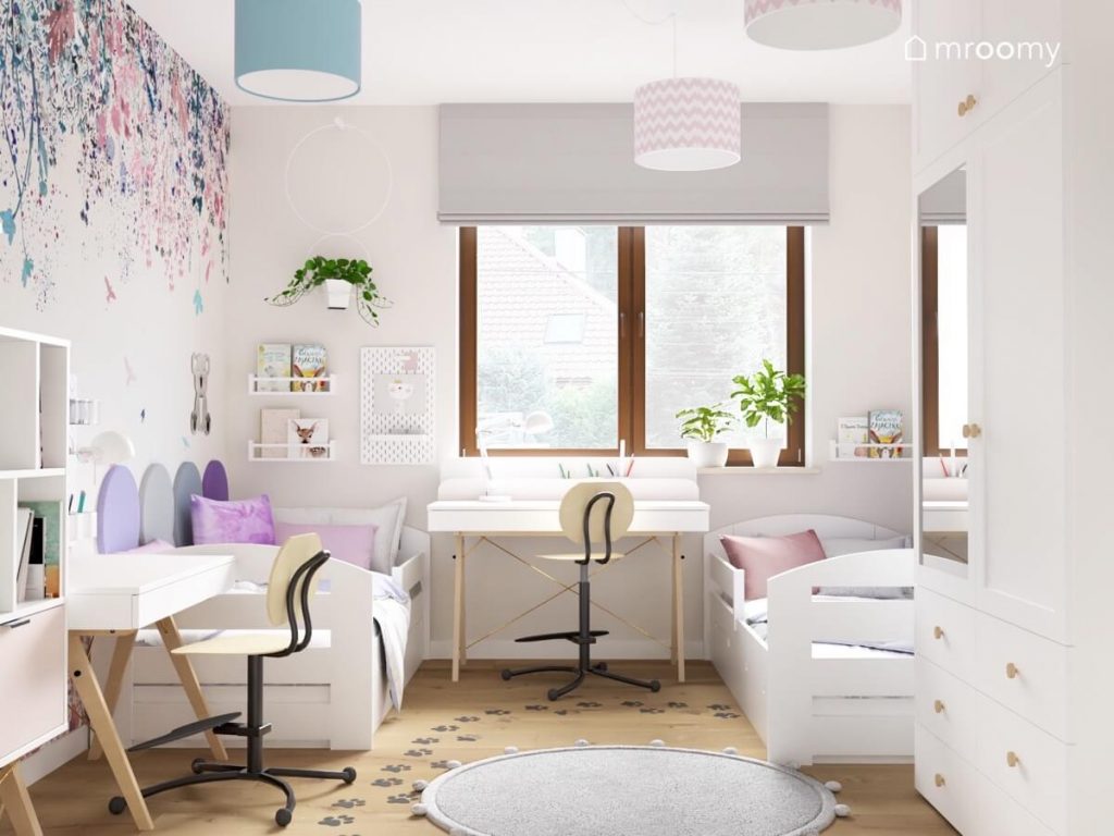 Biały pokój dla dwóch dziewczynek z dwoma białymi łóżkami dwoma biurkami z krzesłami z podnóżkami oraz tapetą w kwiaty na jeden ze ścian i naklejkami podłogowymi w kształcie łapek