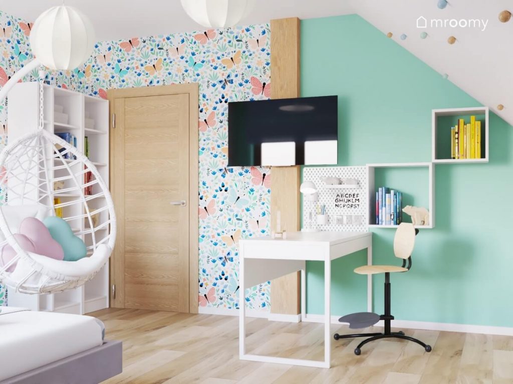 Radosny poddaszowy pokój dla dziewczynki utrzymany w żywych kolorach z tapetą w motyle białymi meblami i telewizorem na ścianie