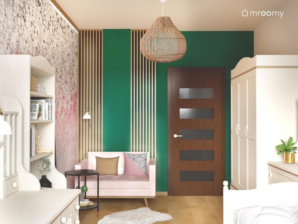 Przytulny pokój dla nastolatki a w nim zielona ściana uzupełniona lamelami różowa kanapa a także białe meble i bambusowe lampy wiszące