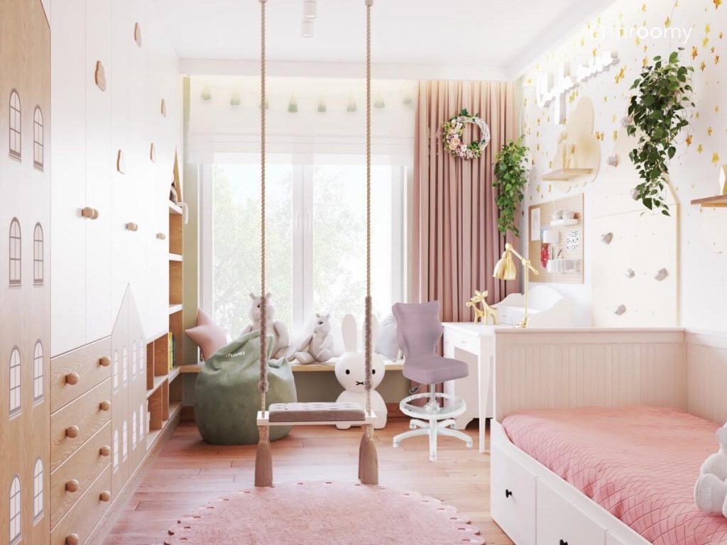 Biało różowy pokój dla dziewczynki a w nim huśtawka wisząca różowe zasłony girlanda pomponów nad oknem oraz biało drewniane meble