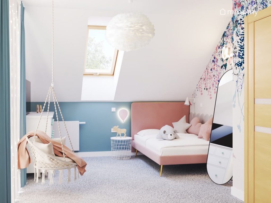 Biało niebieski poddaszowy pokój dziewczynki w wieku szkolnym a w nim różowe tapicerowane łóżko fotel wiszący i podłużne lustro