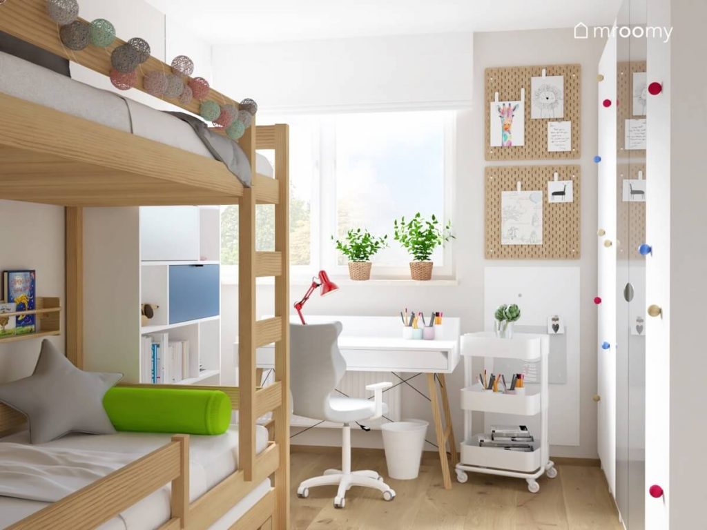 Drewniane łóżko piętrowe a także białe biurko na drewnianych nogach przybornik na kółkach a na ścianie organizery w pokoju rodzeństwa
