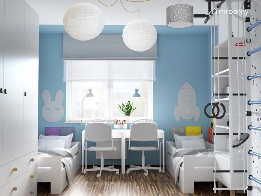 Biało niebieski pokój brata i siostry a w nim dwa białe łóżka dwa biurka drabinka gimnastyczna oraz tablice kredowa w kształcie królika i rakiety
