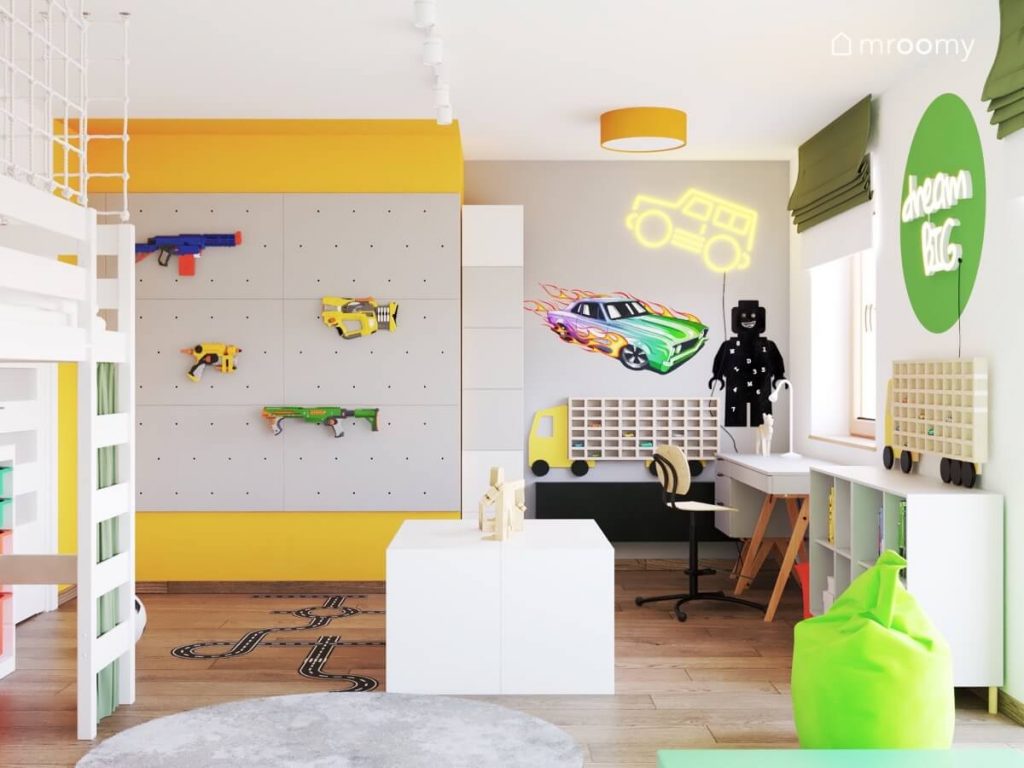 Biało szaro żółty pokój dla chłopca z białymi meblami zielonymi akcentami oraz ścianką organizarem na zabawkowe pistolety i ledonem i naklejką w kształcie auta półką na samochody i tablicą kredową w kształcie ludzika Lego