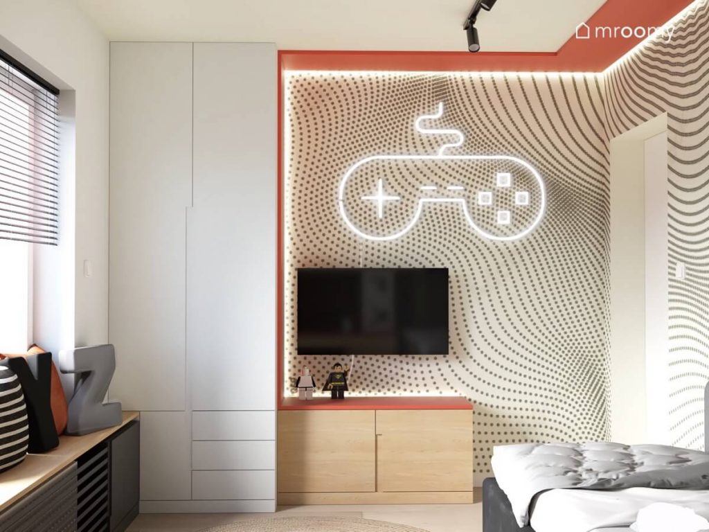 Beżowy pokój dla chłopca z wysoką białą szafą drewnianą szafką telewizorem ledonem w kształcie pada oraz wzorzystą tapetą