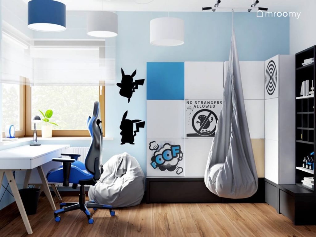 Biało niebieski pokój chłopca w wieku szkolnym z białym biurkiem na drewnianych nogach szafą z nakładkami na fronty szarym fotelem kokonem szarym workiem do siedzenia naklejkami z Pikachu oraz białą szarą i niebieską lampą sufitową