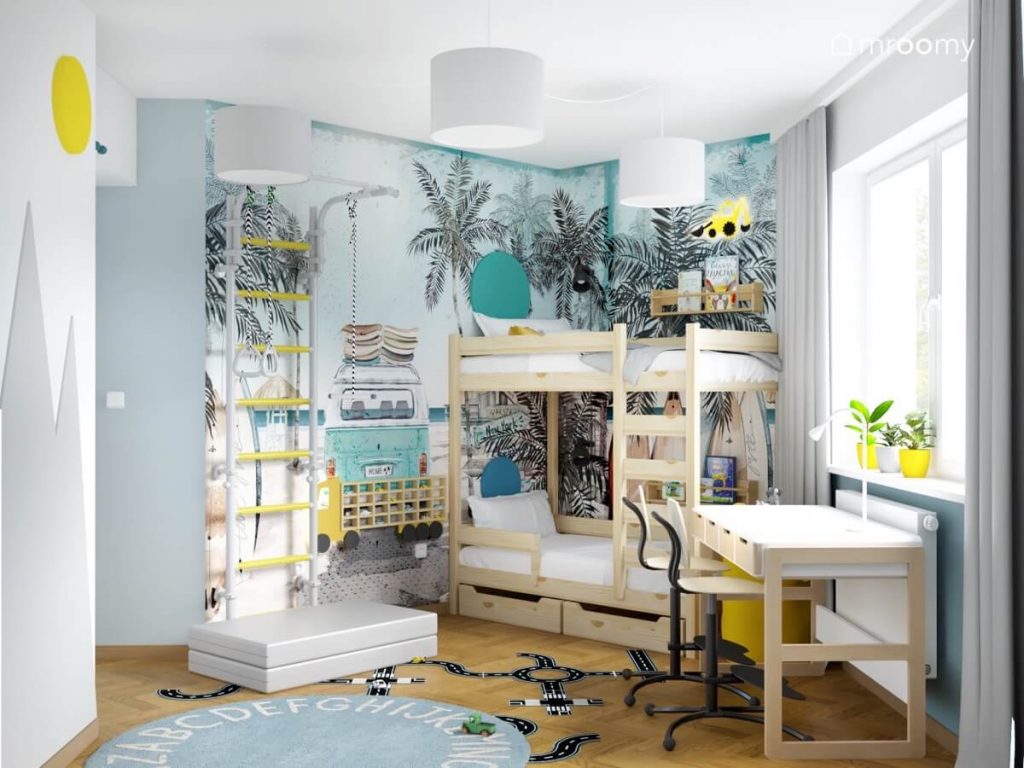 Biało błękitny pokój dwóch chłopców z wakacyjną tapetą a w nim drewniane łóżko piętrowe drabinka gimnastyczna z materacem biało drewniane biurko półka na samochody oraz dywan z alfabetem