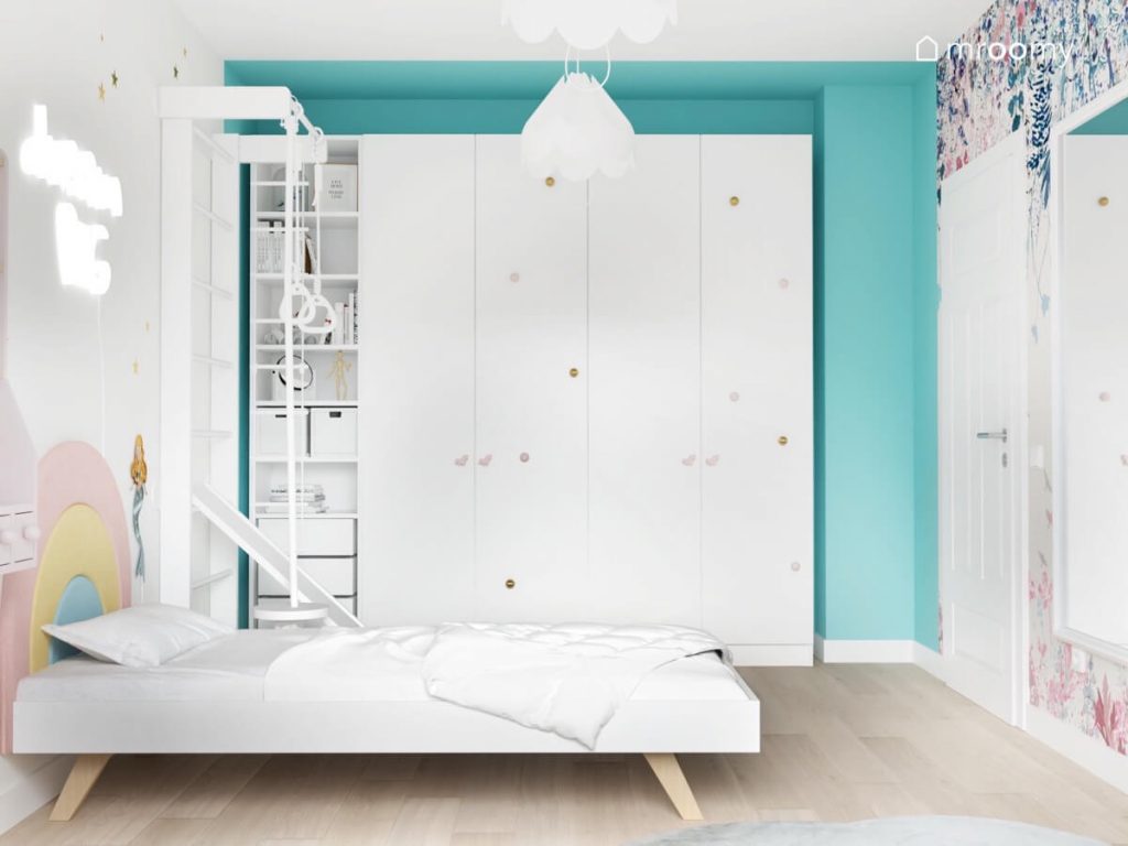 Biało niebieski pokój dziewczynki w wieku szkolnym a w nim białe łóżko drabinka gimnastyczna oraz duża szafa z regałem oraz ozdobnymi gałkami