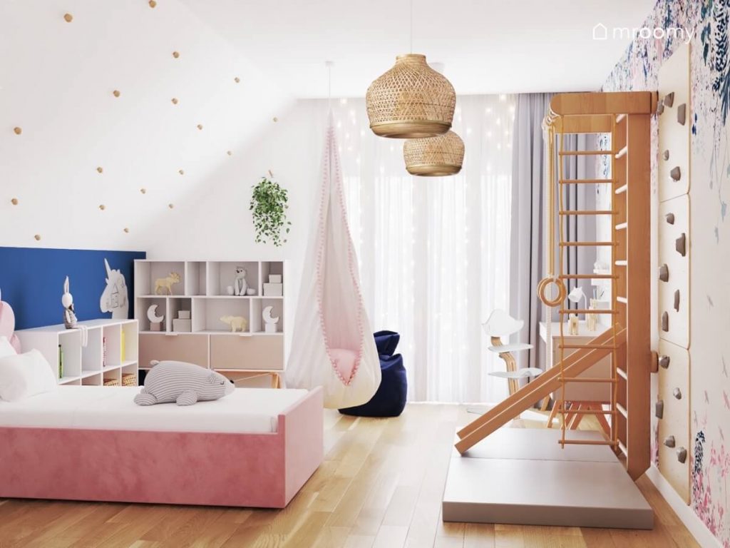 Jasny poddaszowy pokój dla dziewczynki z różowym tapicerowanym łóżkiem drabinką gimnastyczną ścianką gimnastyczną i fotelem kokonem