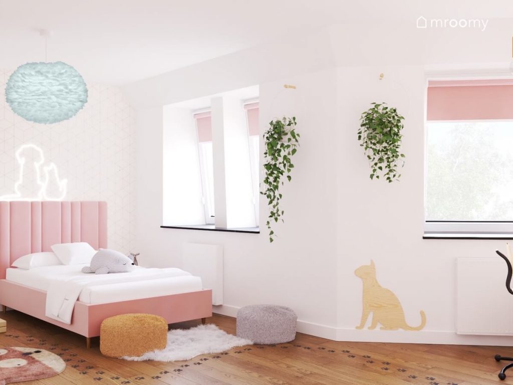 Biały pokój dla dziewczynki z różowym tapicerowanym łóżkiem niskimi pufami ozdobnymi kwietnikami i sklejkowym kotem