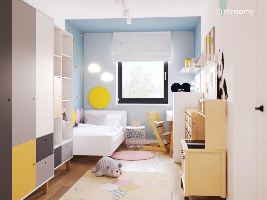 Biało niebieski pokój dziewczynki a w nim białe i drewniane meble kinkiety w kształcie chmurek i miękkie panele ścienne