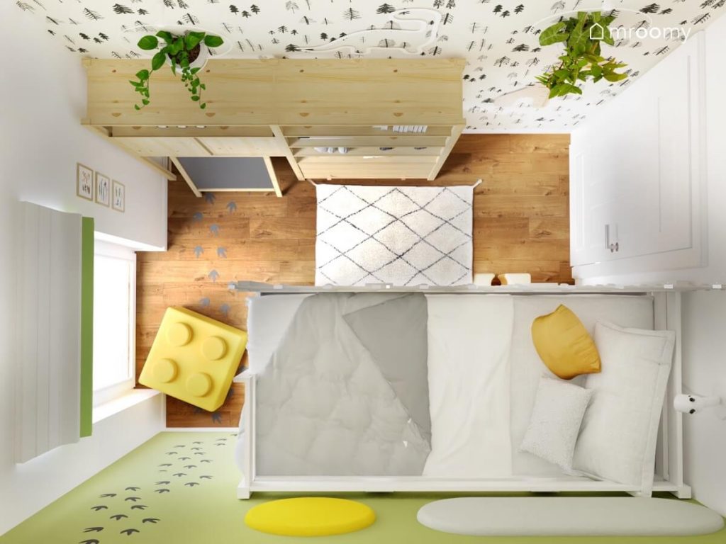 Widok z góry na pokoju dla małego chłopca z drewnianymi meblami łóżkiem na antresoli żółtą pufką w kształcie klocka kwietnikami i białym dywanem z czarnym wzorem