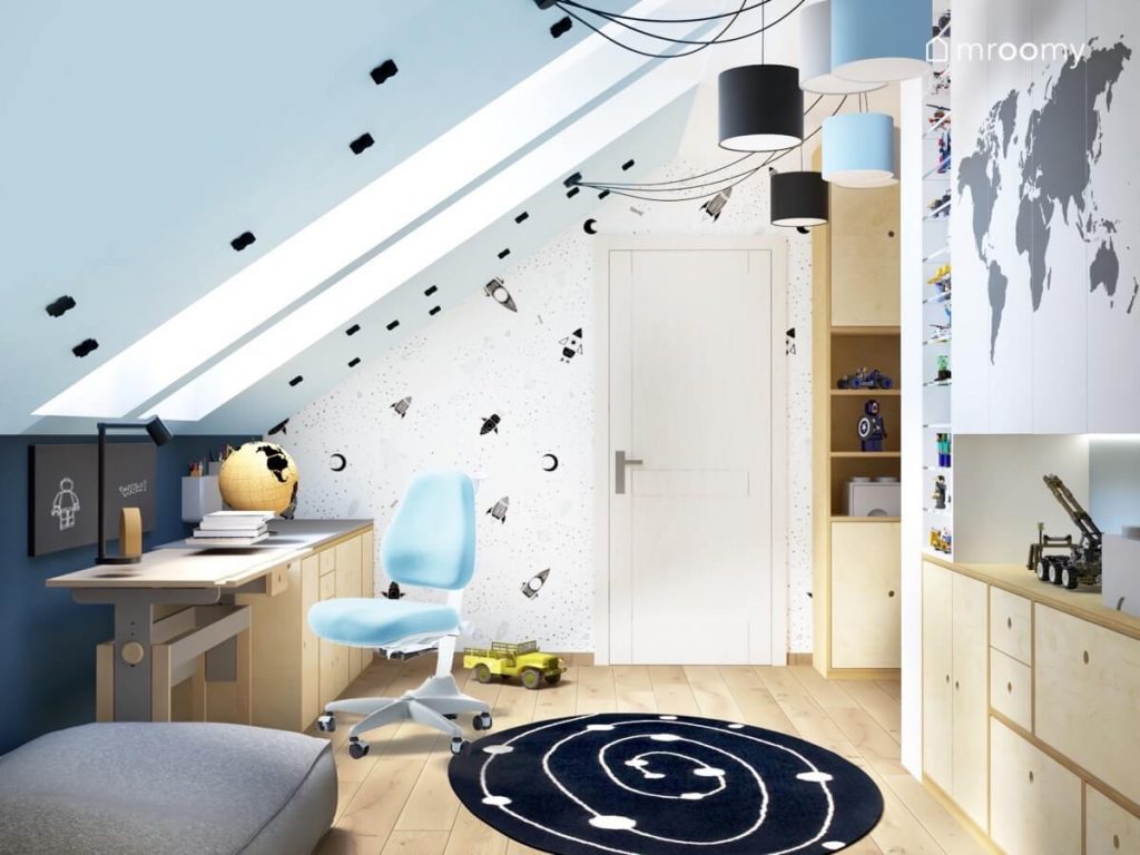 Biało niebieski poddaszowy pokój dla chłopca z drewnianymi meblami galaktycznym dywanem oraz kosmicznymi motywami na ścianie