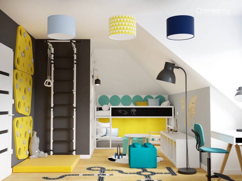 Czarna ściana a na niej biało czarna drabinka gimnastyczna oraz żółte panele wspinaczkowe a także białe łóżko z powierzchnią kredową oraz lampy sufitowe z kolorowymi abażurami oraz lampa podłogowa w pokoju chłopca