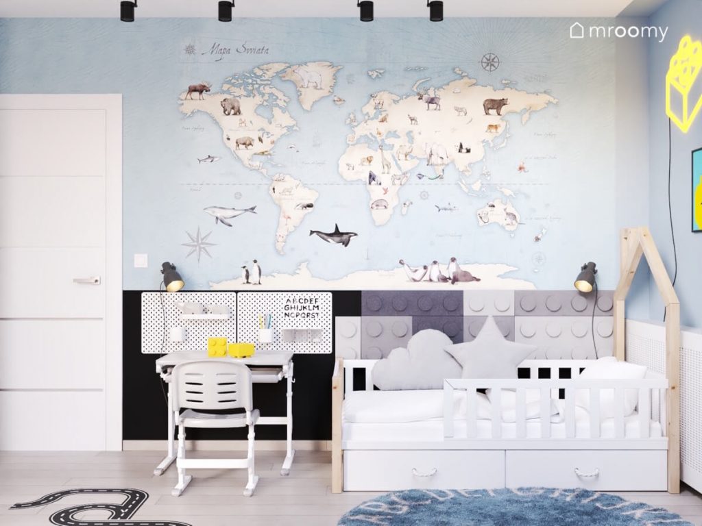 Ściana w pokoju chłopca pokryta tapetą z mapą świata a także biurko z organizerami i łóżko uzupełnione szarymi panelami ściennymi w kształcie klocków