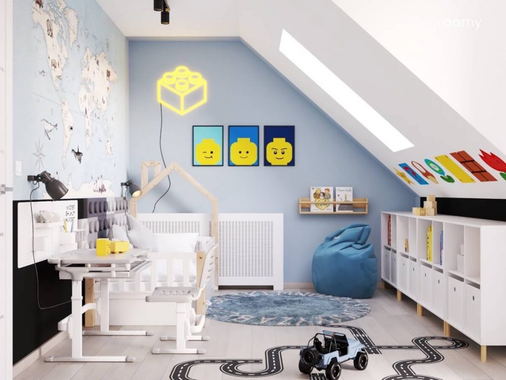 Biało niebieski poddaszowy pokój dla przedszkolaka a w nim białe meble dywan z alfabetem naklejka podłogowa w kształcie jezdni oraz plakaty z Lego oraz ledon w kształcie klocka