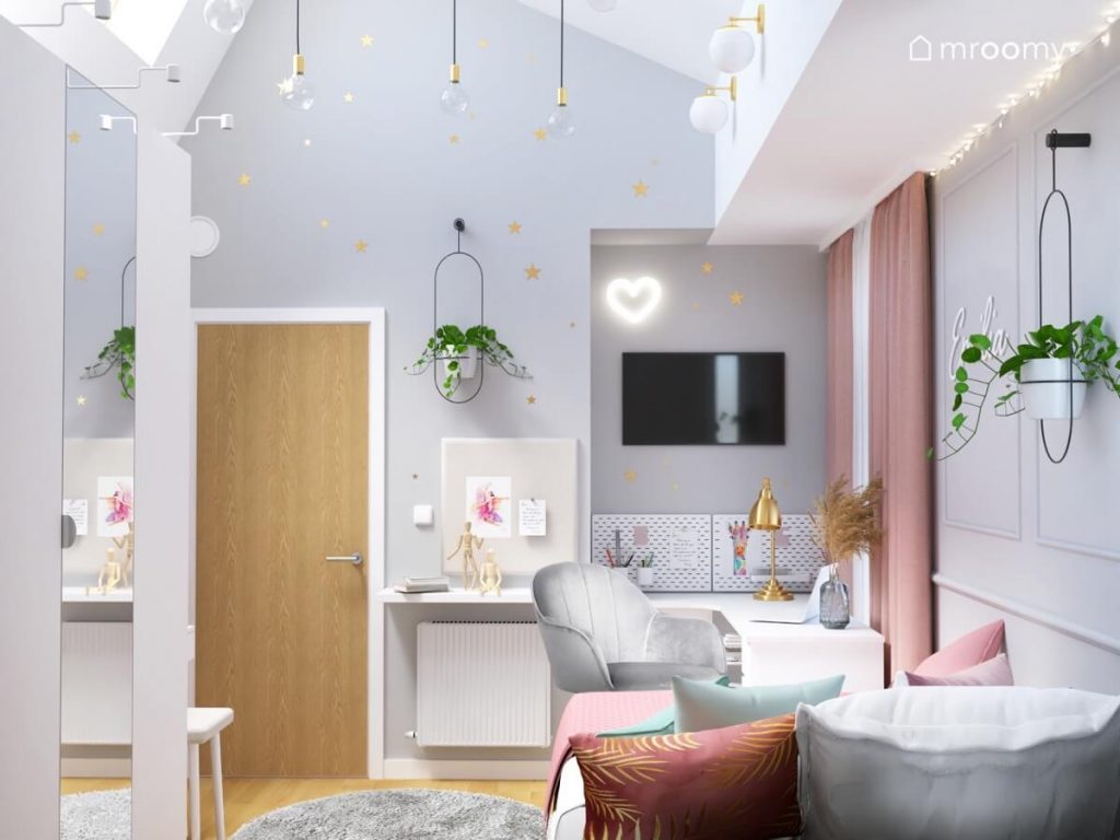 Biało szary wysoki pokój dla dziewczynki w wieku szkolnym a w nim biurko z szarym fotelem telewizor organizery ścienne różowe zasłony kwietnik i złote gwiazdki na ścianie