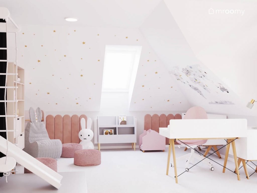 Biały skos w pokoju dziewczynki ozdobiony złotymi gwiazdkami oraz mapą świata a pod nim różowe panele ścienne oraz różowe pufy fotel i lampa w kształcie królika