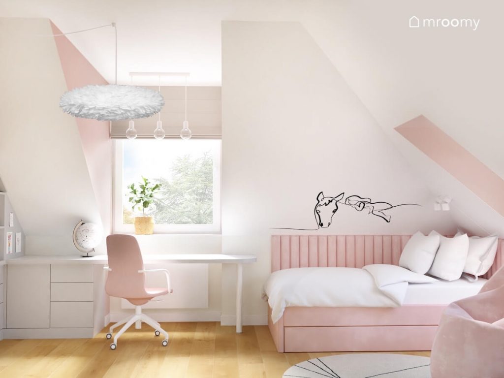 Biało różowy poddaszowy pokój uczennicy a w nim białe biurko z szafką oraz różowe tapicerowane łóżko i naklejka w kształcie konia
