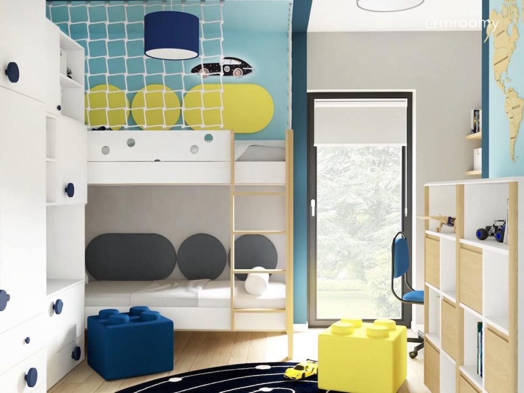 Biało drewniane łóżko piętrowe uzupełnione panelami ściennymi oraz lampką w kształcie wyścigówki a na podłodze pufki klocki w niebiesko szaro białym pokoju chłopca