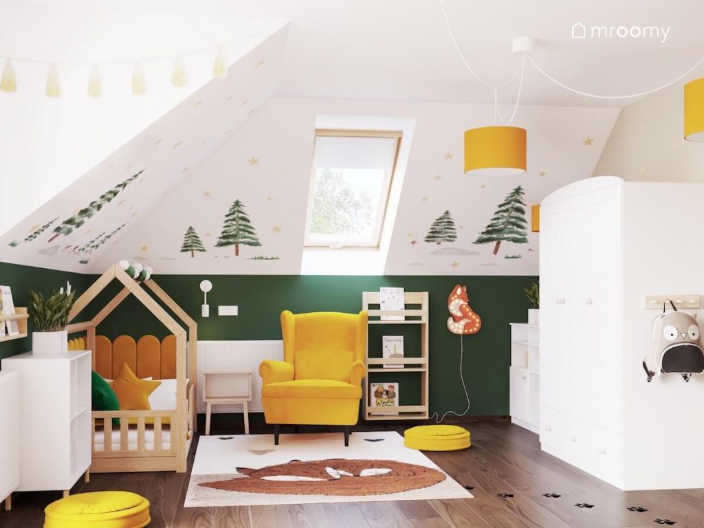Drewniane łóżko domek żółty fotel drewniana biblioteczka i biała szafa a na ścianach choinki i gwiazdki a na podłodze dywan z liskiem w pokoju dziewczynki