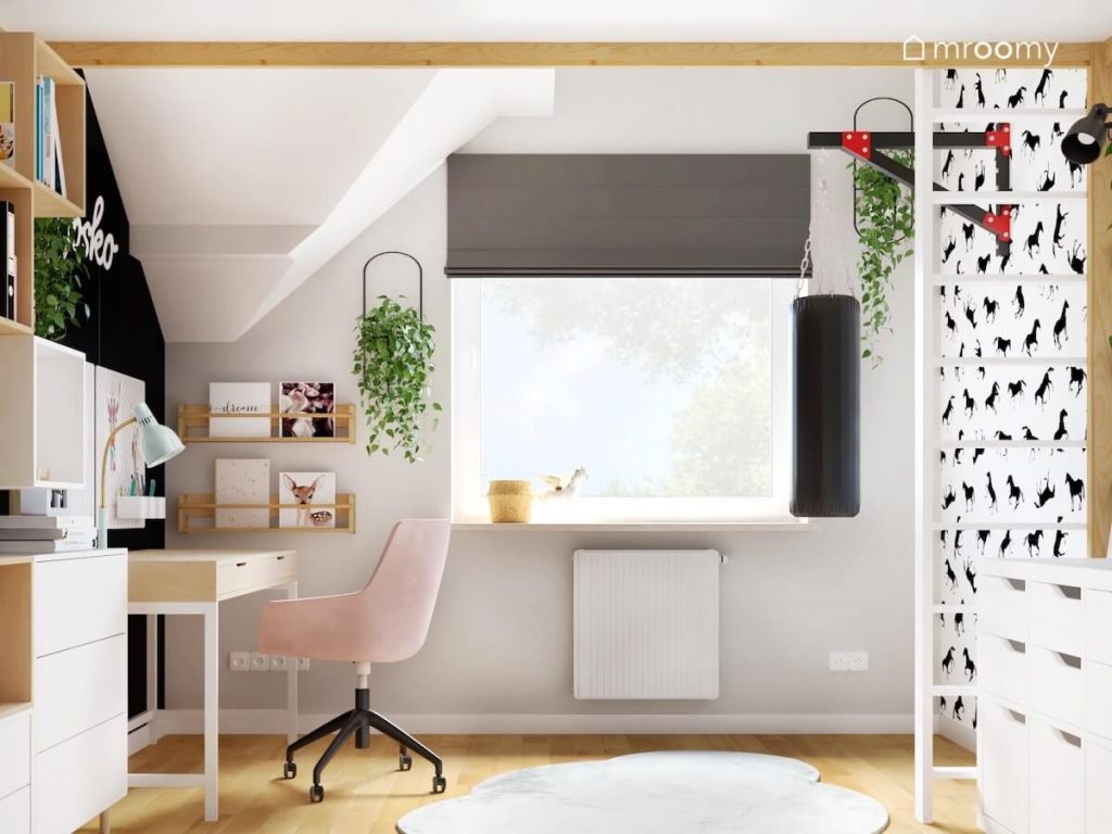 Biało szaro czarny poddaszowy pokój dziewczynki a w nim drewniano białe biurko z różowym krzesłem kwietniki oraz worek treningowy