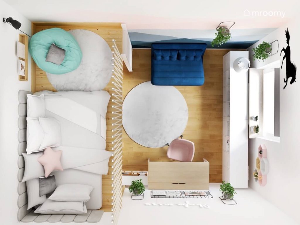 Widok z góry na pokój dziesięcioletniej dziewczynki a w nim drewniane biurko niski biały regał granatowa kanapa oraz łóżko i pufa na antresoli