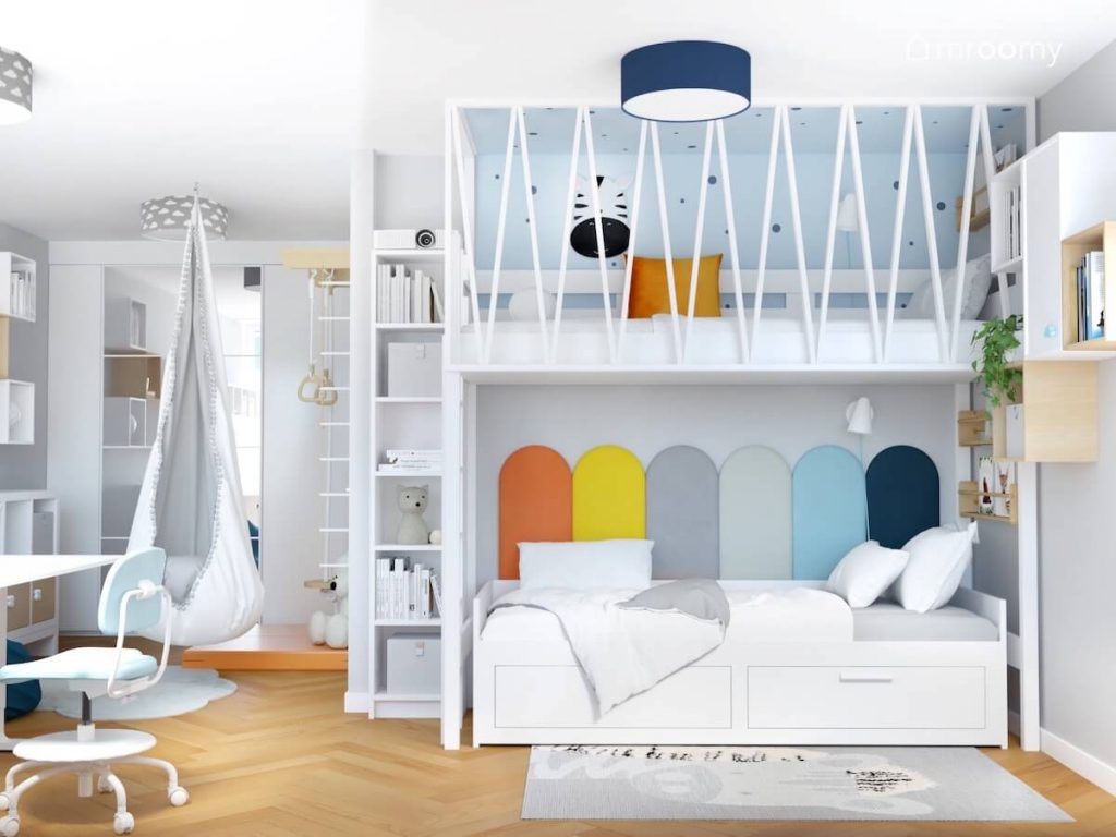 Białe łóżko uzupełnione kolorowymi panelami ściennymi a nad nim antresola a obok wąski regał i fotel kokon w pokoju rodzeństwa