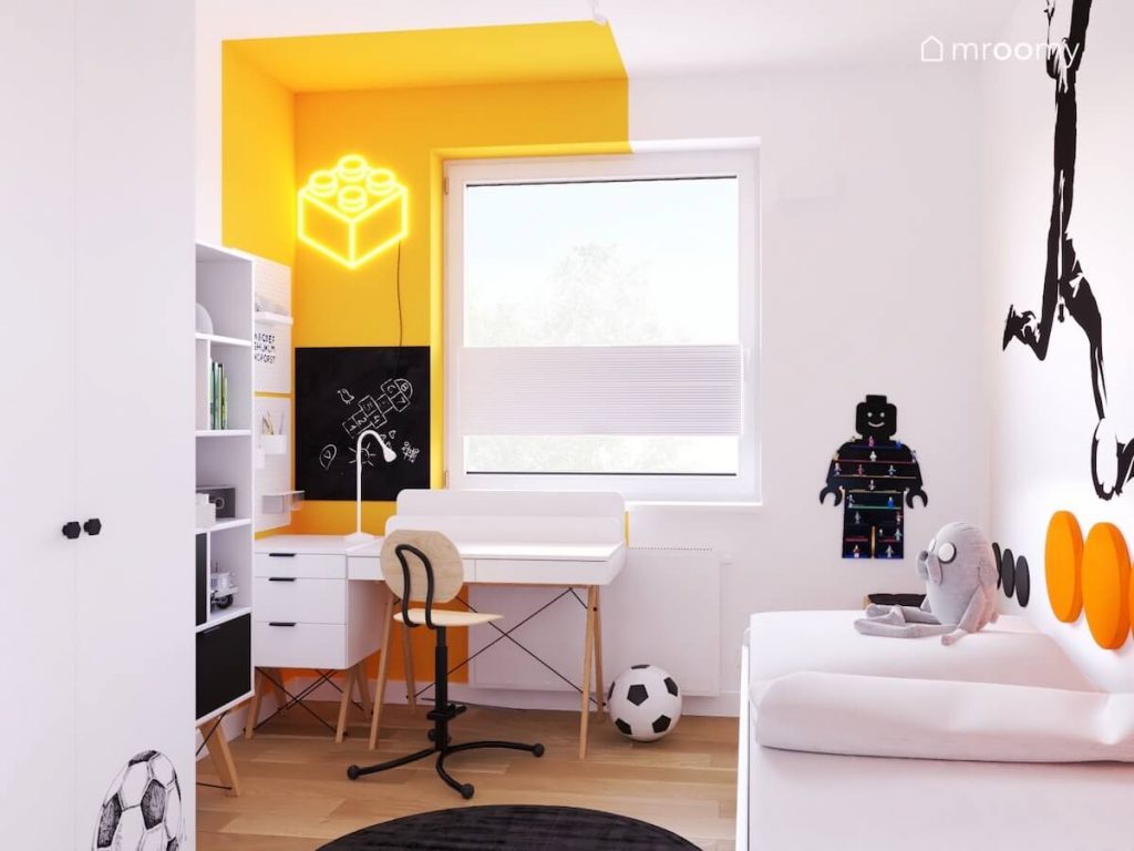 Jasny pokój dla chłopca a w nim białe meble z drewnianymi elementami tablice kredowe oraz naklejka ścienna z piłkarzem i żółty ledon klocek